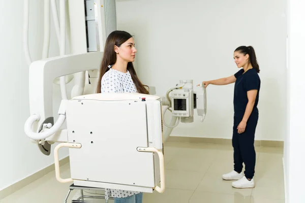 Side view of a female technician giving instructions to a latin young woman standing still for an x-ray at the diagnostic imaging center