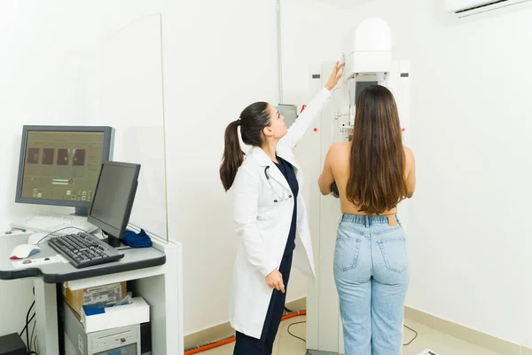 Female technician wearing a lab coat doing a breast mammogram exam on a young woman at the medical diagnostic center