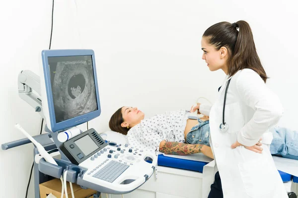 Female doctor doing an ultrasound diagnostics on a pregnant woman and checking her belly at the hospital