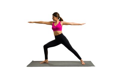 Active hispanic woman in her 20s with a healthy lifestyle practicing yoga and doing a warrior 2 pose against a white background
