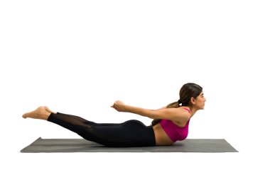 Attractive sporty woman working out with yoga exercises and practicing a locust pose against a studio background