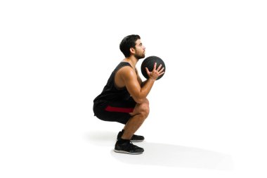 Attractive young man doing squat exercises and using a slam ball during his cross-training workout