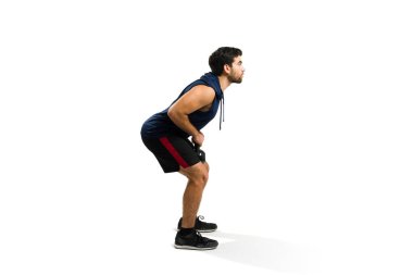 Fit young man working out with a kettlebell weight while doing squat exercises isolated on a white studio background