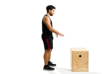 Sporty man preparing to jump on a plyo box during his cross training workout in front of a white background