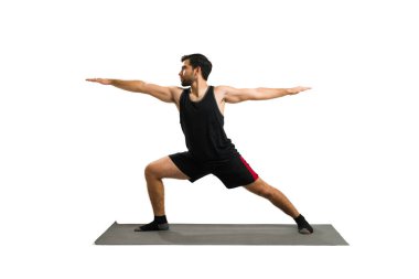 Active hispanic man in his 20s with a healthy lifestyle practicing yoga and doing a warrior 2 pose against a white background