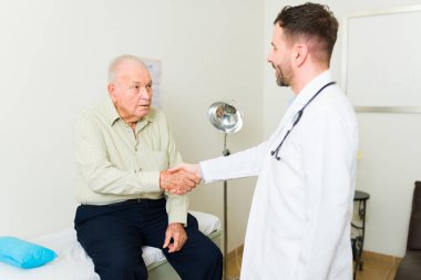 Ill elderly retired man coming into the doctor's office and shaking hands with the geriatrician before his medical exam