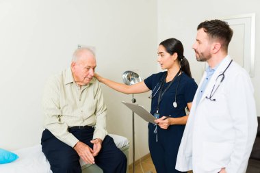 Sick older man in his 80s coming into the doctor's office with a nurse for a medical health check up 