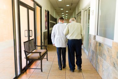Rear view of a caucasian doctor and elderly mature retired man walking together at the retirement home