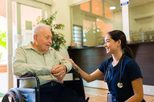 Caring female nurse smiling to a happy elderly mature man on a wheelchair arriving to the retirement hom