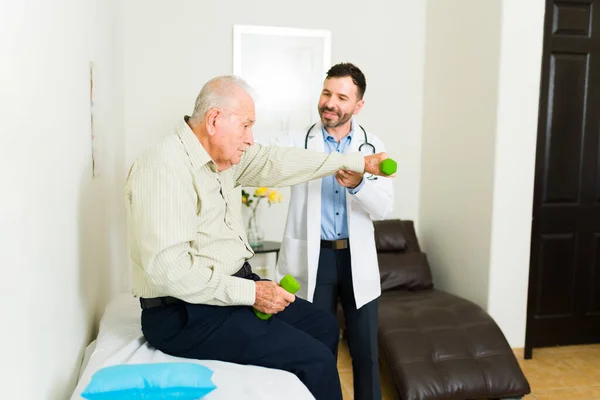 Happy doctor doing a medical check up at his office to an elder old man in his 80s using dumbbells