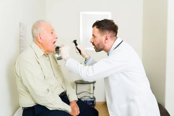 Side view of a doctor geriatrician using an otoscope to check the health of an ill mature old man at the nursery home