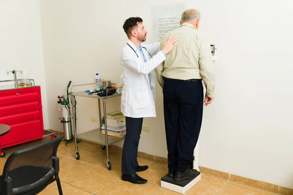 Doctor geriatrician and sick mature elder patient seen from behind at the scale making a medical examination