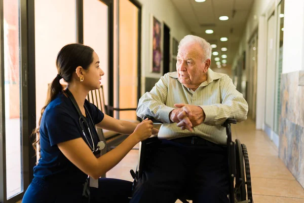 Loving patient nurse comforting while talking with a elder mature man in his 80s on a wheelchair staying at the nursing home