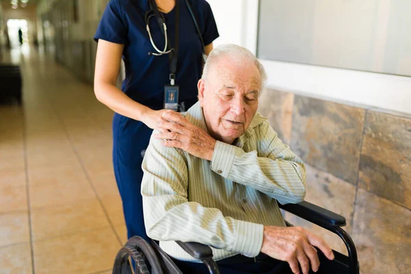 Close up of a caring nurse at the retirement home comforting and putting a hand on the shoulder of relaxed retired old man