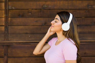 Rahatlamış, güzel bir kadının profili kulaklıkla müzik dinlerken ahşap bir kapının önünde yürüyor.