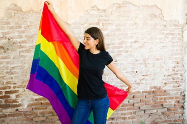 Siyah tişört giyen çekici genç bir kadın gey haklarını ve LGBT topluluğunu desteklemek için gökkuşağı gurur bayrağı sallıyor. 