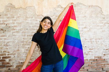 LGBT topluluğunu desteklerken elinde gökkuşağı gurur bayrağı tutan ve gülen eşcinsel bir kadın siyah bir tişört giyiyor.