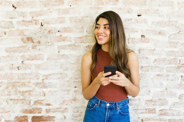 漂亮的年轻女子靠在有复制空间的砖墙上 一边在户外玩耍 一边用智能手机发短信 — 图库照片