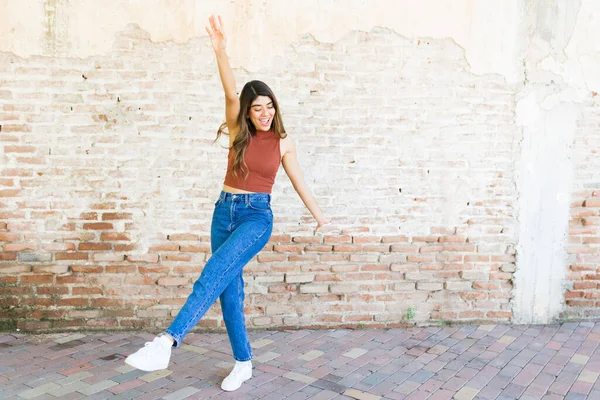 レンガの壁の前で屋外で楽しい時間を過ごしながら笑ったり踊ったりする興奮した若い女性 — ストック写真