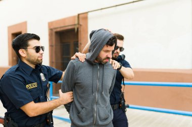 İki polis memuru bir şüpheliyi tutuklayıp karakola getiriyor. 