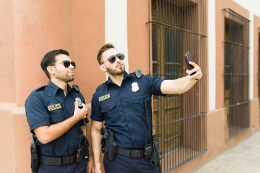 Görevdeki çekici polis ajanları gülümsüyor ve dışarıda mutlu görünüyorlar. Akıllı telefonla selfie çekiyorlar.