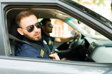 Güneş gözlüklü bir polis memuru, bir şüpheliyi arıyor ve polis arabasında dolaşırken, sokaklarda kanunları uyguluyor.