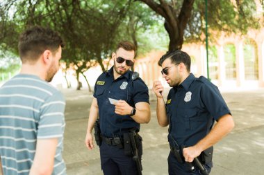 Siyah üniformalı ve güneş gözlüklü iki polis bir şüphelinin kimliğini doğrularken telsizle konuşuyor.