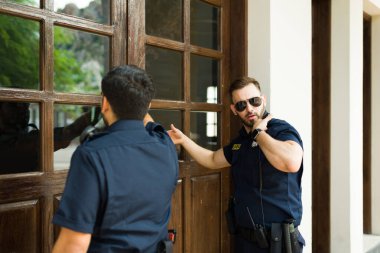 Beyaz erkek polis, soruşturma yapmak ve suç delillerini aramak için arama emriyle evin kapısını çalıyor.