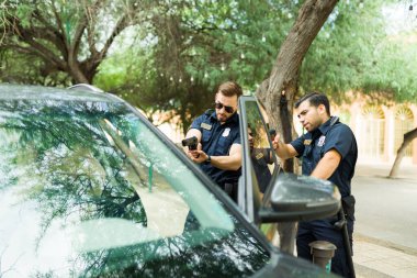 Görevli polis memurları tutuklama yapıyor ve soruşturmadan sonra araba kullanan bir suçluya silah doğrultuyorlar.