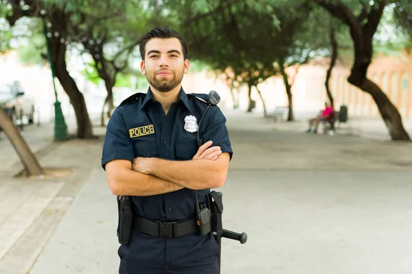 Police agent on duty wearing a black uniform crossing his arms while preventing crime while standing in the park