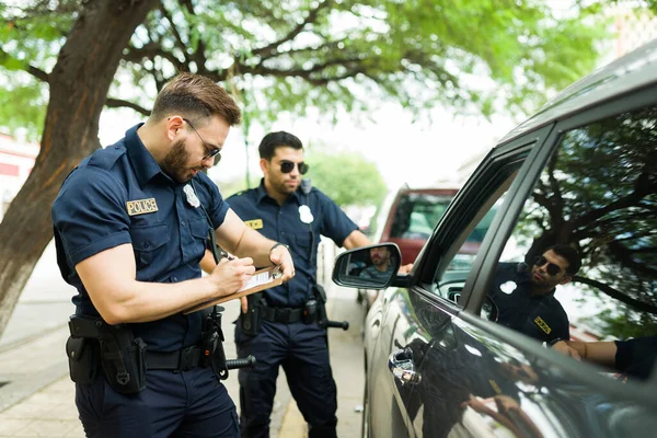 Two police officers with sunglasses giving a traffic ticket or fine to a driver for violating parking or speeding