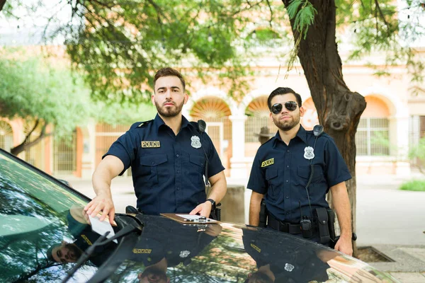 Portrait of attractive police officers looking at the camera while putting a traffic parking ticket on a car