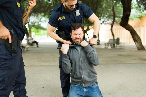 Angry young man criminal resisting the arrest while trying to escape of the police officers and fighting a cop using a baton