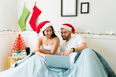 Noel Baba şapkalı, gülümseyen ve internette Noel alışverişi yapan güzel bir çift.