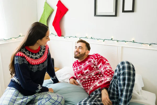 Happy couple wearing pajamas and christmas sweaters relaxing in bed together in the morning
