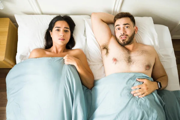 Concerned young couple in the morning looking surprised of having sex together and sleeping in bed