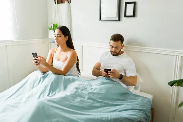 夫妻俩在床上醒来后 一边用智能手机发短信 一边显得很无聊 这让他们很不爽 — 图库照片