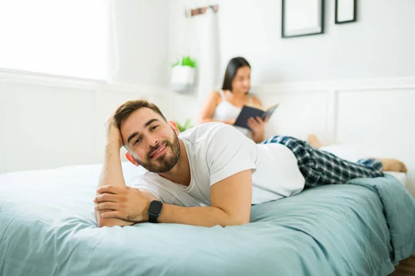 Handsome young man in pajamas making eye contact smiling while relaxing on a leisure day in bad with his wife or girlfriend