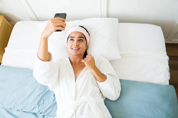 迷人的惊慌失措的女人在床上笑着 用智能手机拍了一张性感的照片发给男友 — 图库照片