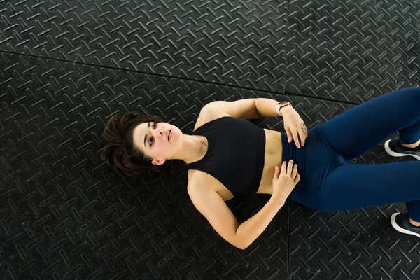 Top view of an exhausted woman looking tired while resting and lying on the floor at the gym after a cardio workout