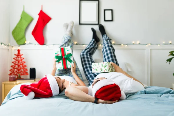Расслабленная Молодая Пара Шляпах Санта Клауса Открывает Подарки Отдыхая Ногами — стоковое фото