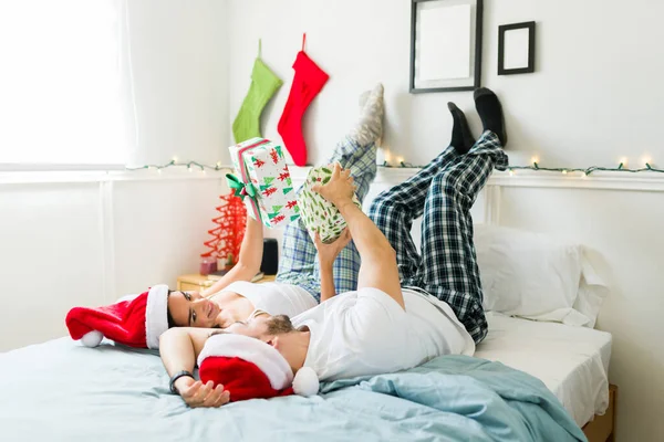 Веселая Красивая Пара Обменивается Рождественскими Подарками Поднятыми Ногами Постели Расслабляясь — стоковое фото
