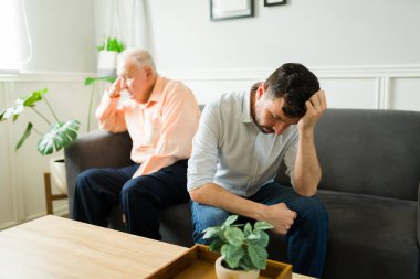 Oturma odasındaki kanepede otururken yaşlı babasıyla tartıştıktan sonra üzgün görünen bunalımlı beyaz bir adam.