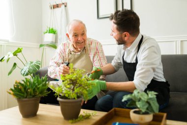 Kafkasyalı oğluyla konuşurken gülümseyen ve evdeki çiçeklerle uğraşan heyecanlı yaşlı bir adam.