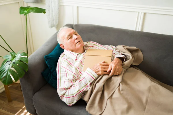 Vyčerpaný Starší Muž Usíná Gauči Dekou Zatímco Čte Knížku Odpočívá — Stock fotografie