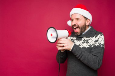 Kırmızı arka planda Noel tatilinin tadını çıkarırken megafonla bağıran heyecanlı mutlu adam.
