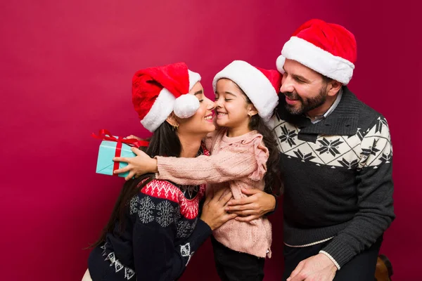 サンタの帽子を持つ家族を愛する彼らのかわいい娘を抱きながらクリスマスプレゼントを開く — ストック写真