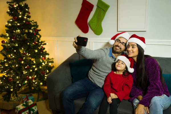 自宅でクリスマスを祝いながら 女の子がソーシャルメディアのためにスマートフォンを使用して自撮りしている陽気な家族 — ストック写真