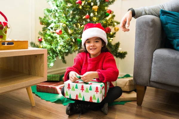 Spanisches Kleines Mädchen Mit Weihnachtsmütze Sitzt Vor Dem Weihnachtsbaum Und — Stockfoto