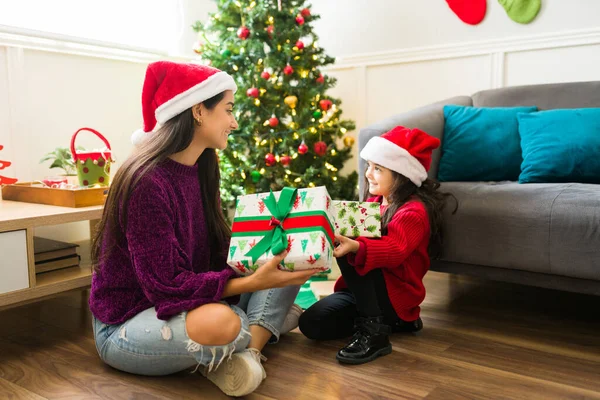 ラテン若いです女性と小さな子供とともにサンタ帽子笑顔とオープニングギフト下ザクリスマスツリー — ストック写真